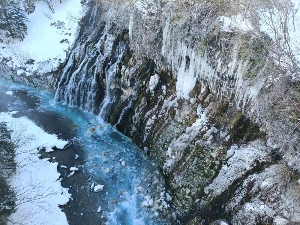 Frozen waterfall with icicles and turquoise stream below